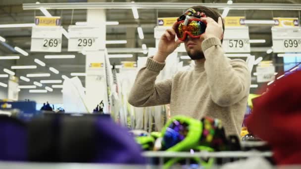 Молодой человек выбирает очки для сноуборда в гипермаркете . — стоковое видео