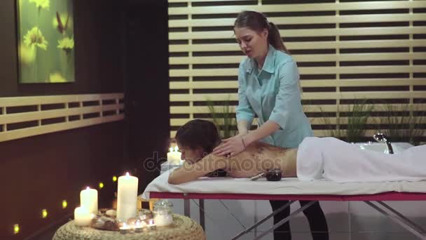 De masseur zet een scrub op de achterkant van de meisjes om te helpen de huid zachter geworden. — Stockvideo