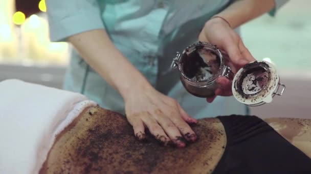 Close up tiro das mãos massagistas aplicando uma esfoliação de café para o corpo da mulher . — Vídeo de Stock