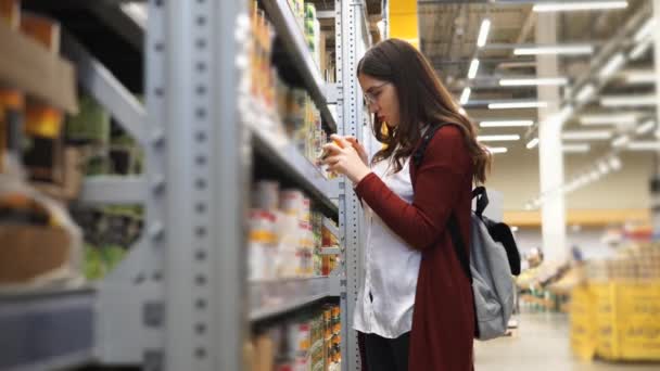 Jovem mulher escolhendo jarros de milho em um hipermercado . — Vídeo de Stock