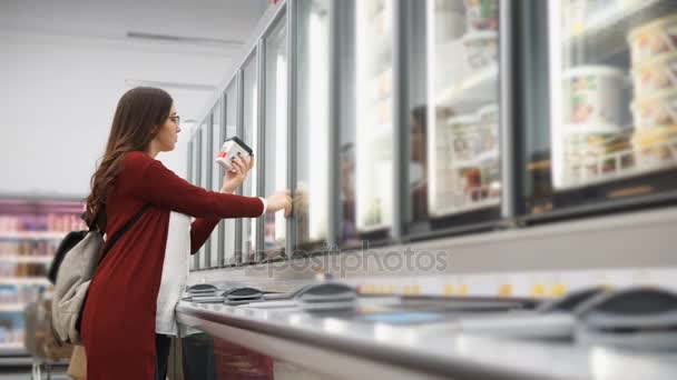 Woman with a backpack chooses products from the refrigerator in the supermarket. — Stock Video