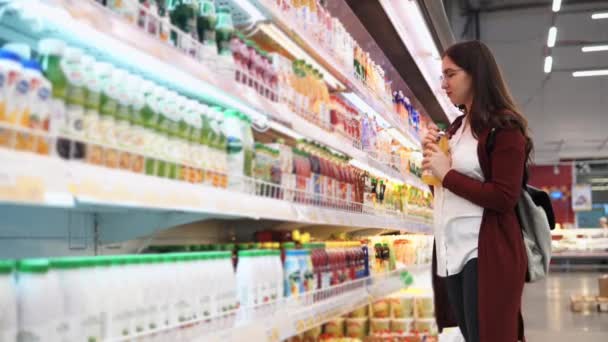 Jovem escolhe bebidas no supermercado, olhando para a composição . — Vídeo de Stock