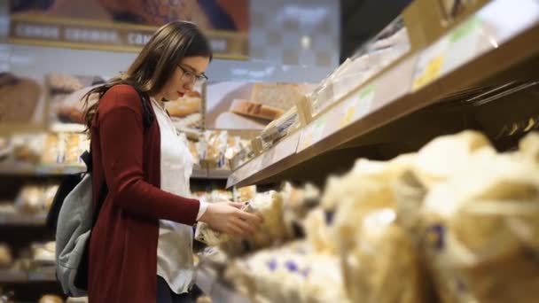 Giovane donna con gli occhiali che odora di pane fresco al supermercato . — Video Stock