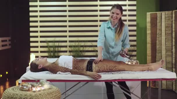 Een vriendelijke masseuse toepassen een voorontwerp peeling om chocolade wrap. — Stockvideo