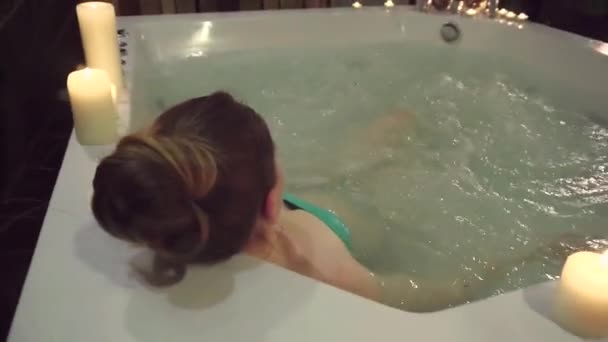 A woman takes a jacuzzi in a spa, enjoying aromatic candles and silence. — Stock Video