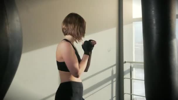 Mujer deportiva se dedica al boxeo, trenes con una bolsa de boxeo en el gimnasio — Vídeos de Stock