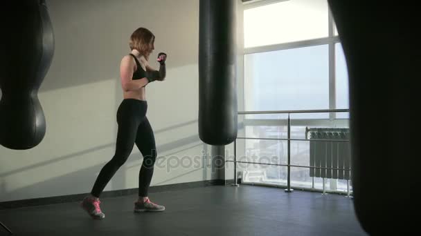 Una mujer en un traje deportivo cumple un golpe de boxeo en un equipo deportivo — Vídeos de Stock