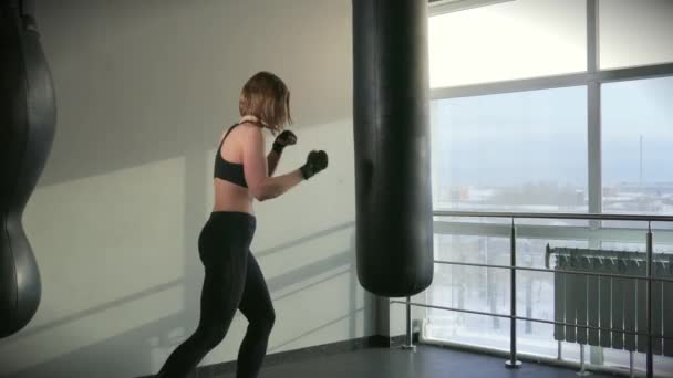 Una mujer en un traje deportivo cumple un golpe de boxeo en un equipo deportivo — Vídeos de Stock