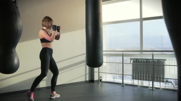 Una mujer en un traje deportivo cumple un golpe de boxeo en un equipo deportivo — Vídeos de Stock