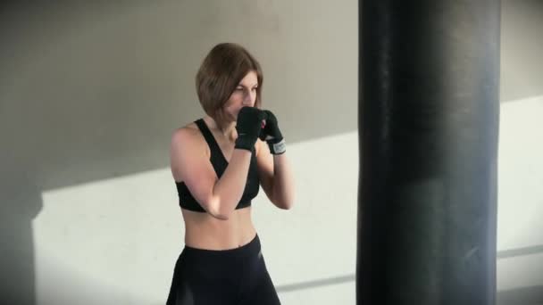La deportista se golpea las manos con confianza en la bolsa de boxeo del gimnasio — Vídeo de stock