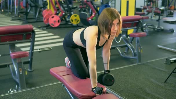 Woman doing exercises for back using dumbbells resting on knee and hand. — Stock Video