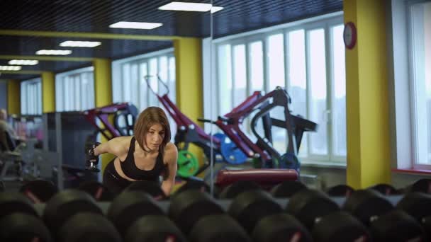 Uma mulher esportiva olha no espelho e bombeia os músculos do antebraço . — Vídeo de Stock