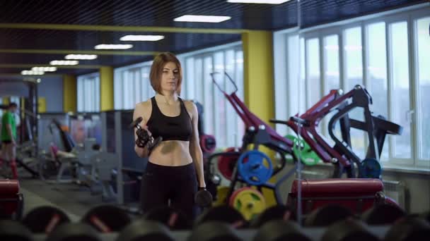 En vuxen idrottskvinna swinging hennes biceps på armarna i ett gym. — Stockvideo