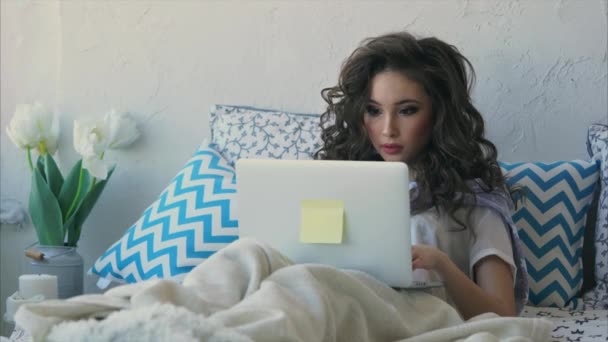 Mladá žena nedávno se probudil v posteli a kontroluje poštu na přenosném počítači. — Stock video