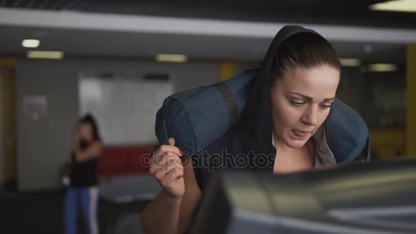 Woman is engaged in fitness on treadmill, she is holding a bag on her shoulders. — Stock Video