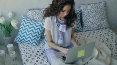 Genç Moda blogger yatakta oturmuş bir dizüstü bilgisayarda yeni bir makale yazıyor.
