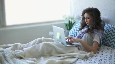 Genç kadın yalanlar üzerine bir yatak yatak odası ve Internet üzerinde arkadaşlarınızla sohbet.