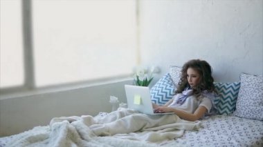 Genç kadın sosyal ağlar bir dizüstü bilgisayarda Internet üzerinde seyrederken yatakta dinleniyor.
