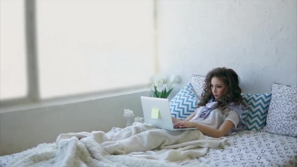 Junge Frau liegt im Bett und schaut sich auf einem Laptop soziale Netzwerke im Internet an. — Stockvideo