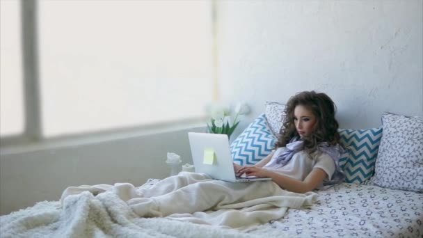 Pretty woman lies in on bed and works on laptop in the morning. — Stock Video