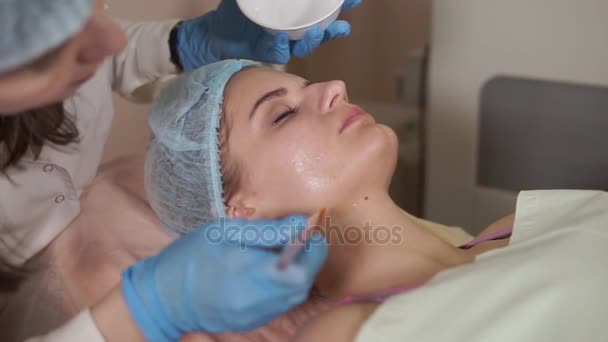 Косметолог надевает маску для лица на пациентку. Омоложение косметологии . — стоковое видео