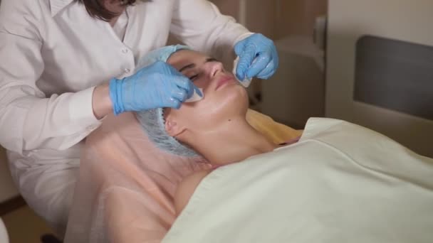 Процедура красоты. Красавчик снимает маску с лица пациентки . — стоковое видео
