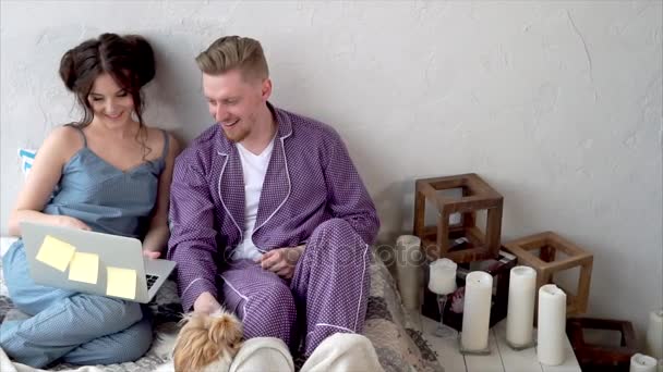 Mann und Frau mit Notizbuch shoppen online und spielen mit Hund im Bett — Stockvideo