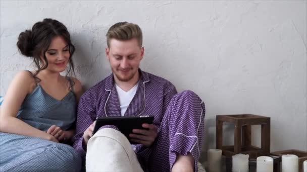 Любляча пара в піжамі, виберіть готель на планшеті для відпочинку . — стокове відео