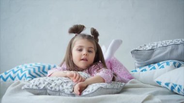 Küçük kız yatakta ve düşünceli ayaklarını sallayarak üzerinde şirin pijama