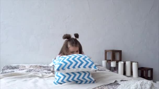 Una chica dulce y alegre juega con almohadas en la cama en el dormitorio . — Vídeos de Stock