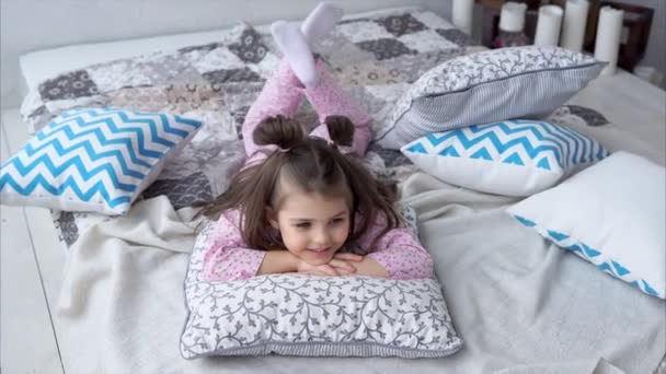 Una chica dulce y alegre juega con almohadas en la cama en el dormitorio . — Vídeos de Stock