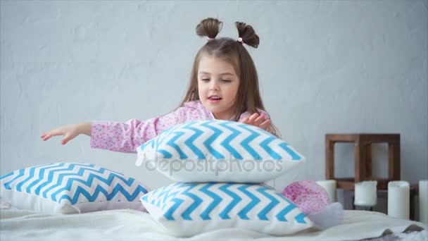 Een klein meisje in haar huis pyjama zet een piramide van kussens in haar slaapkamer. — Stockvideo