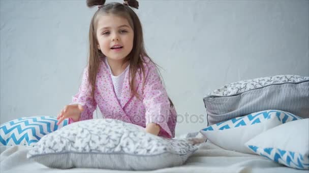 Чарівна маленька дівчинка в рожевій піжамі прокинулася в ліжку. Щаслива дитина . — стокове відео