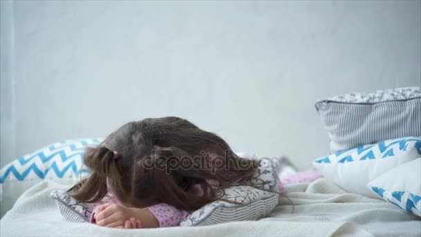 Dulce niña feliz en pijama rosa acostada en la cama sobre almohadas . — Vídeos de Stock