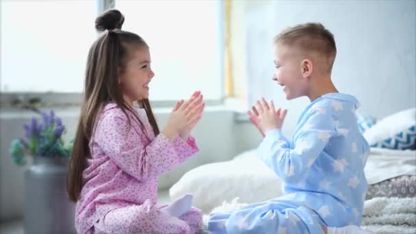 Precioso niño y niña vestidos con pijamas caseros jugar el juego en sus manos — Vídeos de Stock