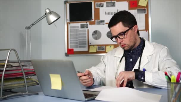 Ένας νεαρός γιατρός υπογράφει έγγραφα στο τέλος της ημέρας στο πολυϊατρείων — Αρχείο Βίντεο