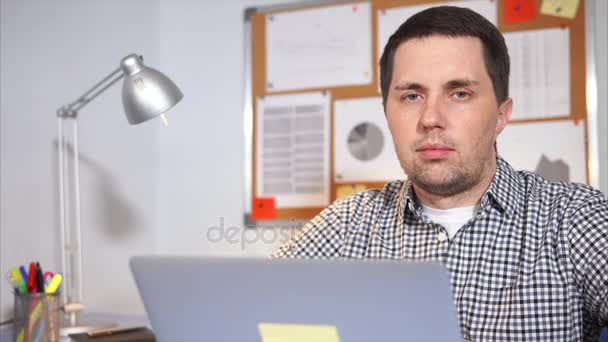Egy egyszerű ember nézi a kamera, előtte áll egy hordozható laptop — Stock videók
