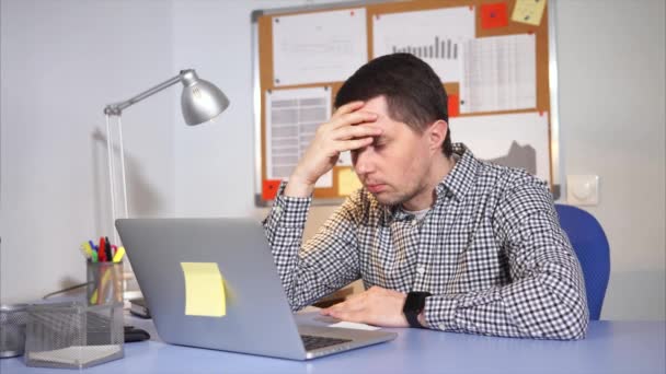 O administrador de rede cansado se apega à cabeça e trabalha em um laptop — Vídeo de Stock