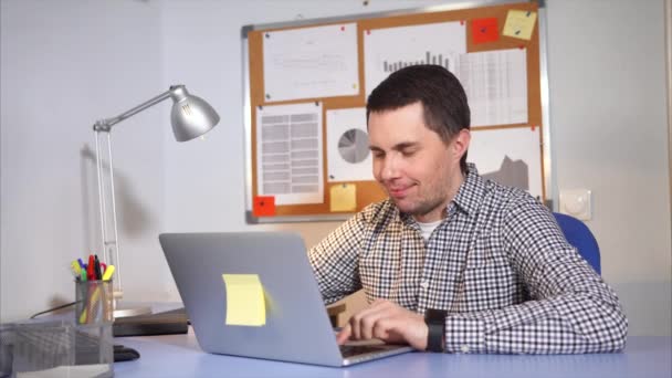Un hombre satisfecho mira el monitor del portátil y escribe un mensaje a un amigo — Vídeo de stock