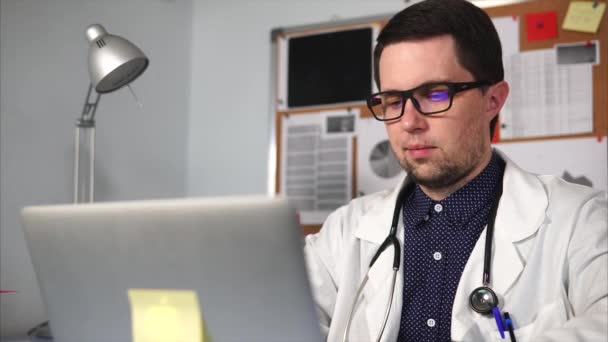 Doctor de una clínica privada imprime el texto en el portátil en su oficina privada — Vídeos de Stock