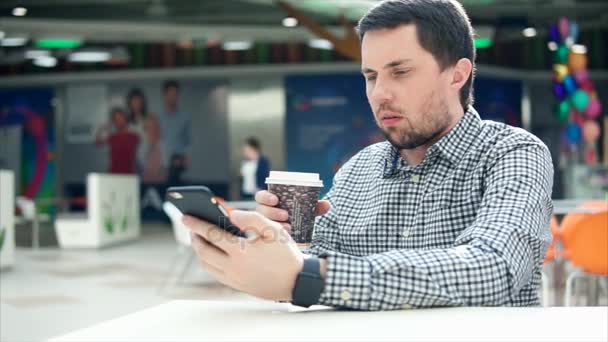 Мужчина с сосредоточенным взглядом печатает смс на мобильном телефоне, в руке кофе . — стоковое видео