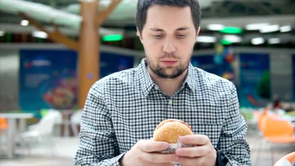 Mladý muž je jíst hamburger s masem v potravinách soudu. — Stock video