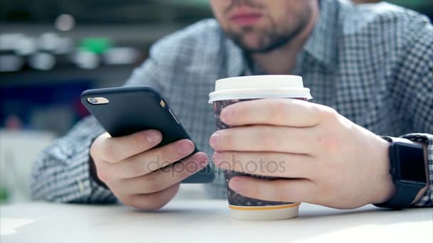 Vista de perto do homem no café usa seu smartphone e segura xícara de café . — Vídeo de Stock