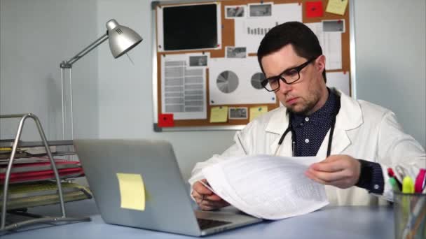 Arzt arbeitet am Arbeitsplatz mit Notizbuch und medizinischen Formularen. — Stockvideo