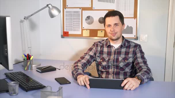Een glimlachende man kijken naar de camera zitten in zijn kantoor — Stockvideo