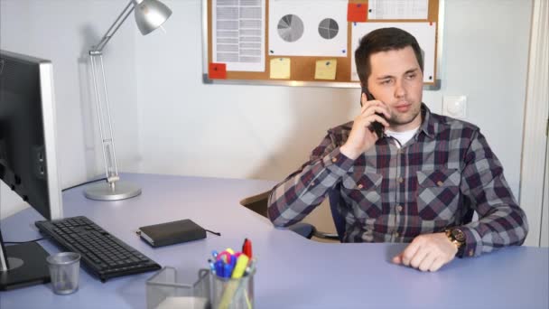 Geschäftsmann verhandelt am Smartphone in seinem Büro, in dem ein Computer steht — Stockvideo