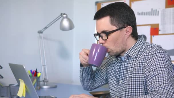 Пользователь мужского компьютера печатает на клавиатуре, смотрит на экран и пьет кофе — стоковое видео