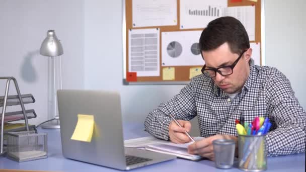 Trabalhador de escritório trabalhando no laptop e escrevendo informações em papéis . — Vídeo de Stock