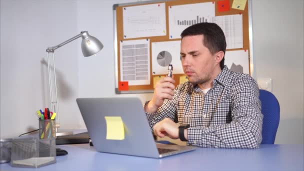 Mladý muž pomocí přenosného počítače v jeho kanceláři. On je vaping. — Stock video