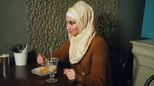 Una mujer musulmana moderna come postre y bebe un cóctel de chocolate en un café — Vídeos de Stock